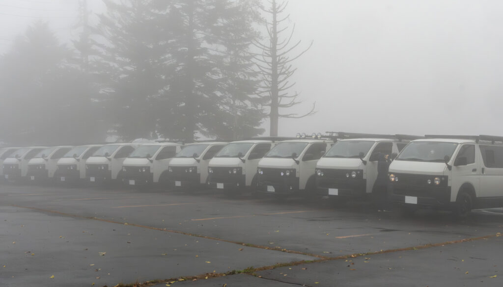 霧の中ずらりと並んだGMLVAN。V-01、V-02、C-01と車種別に整列したGMLVANが霧の中で佇む姿が印象的です。